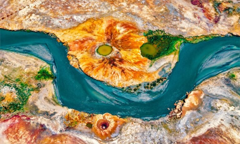 Río sinuoso entre sedimentos dorados y verdes visto desde el aire